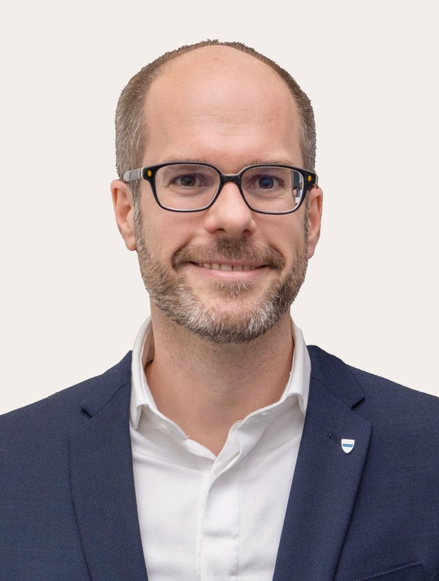 Dr. Ernst Guggisberg Ein Foto von Ernst Guggisberg vor beigem Hintergrund.